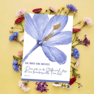 May include: A greeting card with a watercolor illustration of a blue flower with a gold center. The card has German text that reads "DU BIST DIE BESTE!" surrounded by colorful flowers on a yellow background.