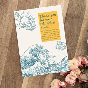 May include: A greeting card with a Japanese wave design in teal and a yellow rectangle with the text "Thank you for your refreshing visit!!" The card also includes a Bible verse. The card is on a wooden surface with flowers and greenery.