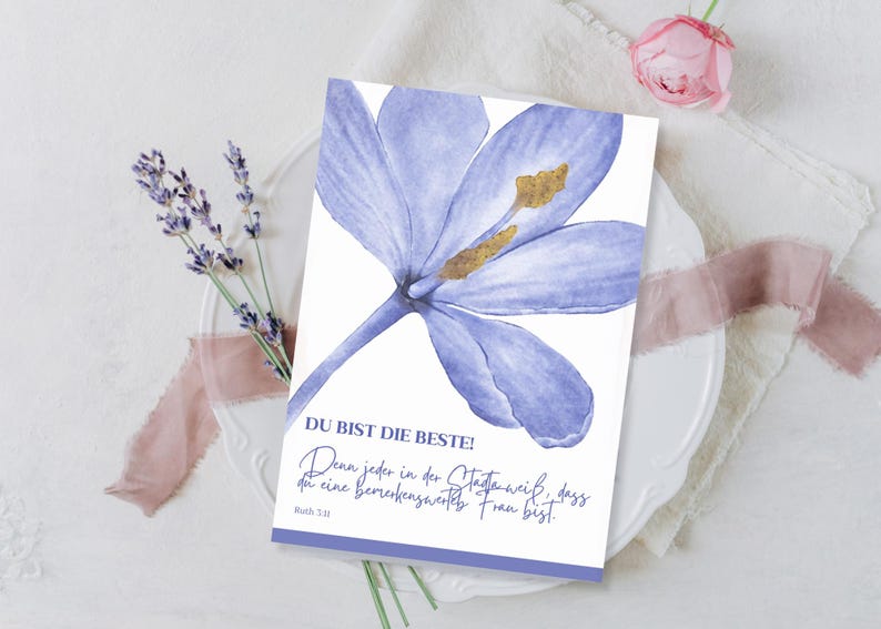 May include: A greeting card with a watercolor illustration of a light purple flower. The card has text in German that reads "DU BIST DIE BESTE!" and a quote. A sprig of lavender and a pink rose are also visible.