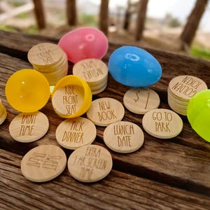 May include: Wooden tokens with various phrases like "Ride Front Seat", "New Book", "Lunch Date", "Go To Park", "Sweet Treat", "Extra 1 Hr Screen Time", "Paint Time", "Pick Dinner", "$1", "Golden Token" and "Ice Cream Date". The tokens are in plastic Easter eggs.