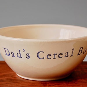 May include: A white ceramic bowl with blue lettering that reads "Dad's Cereal Bowl".