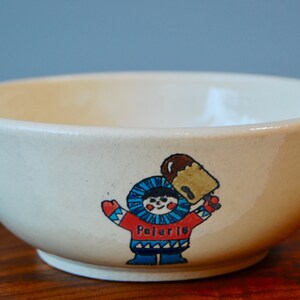May include: A white ceramic bowl with a cartoon illustration of a person wearing a red and blue winter outfit holding a brown ice cream cone. The text "Polaris" is printed below the illustration.