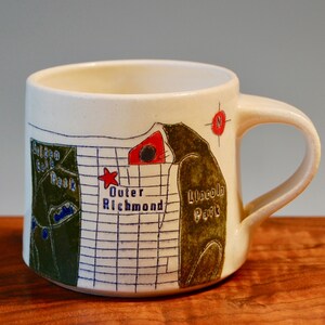 May include: White ceramic mug with a map of Richmond, Virginia printed on it. The map includes the locations of Outer Richmond, Lincoln Park, and the Golden Gate Park. The mug has a handle and a compass rose on the side.
