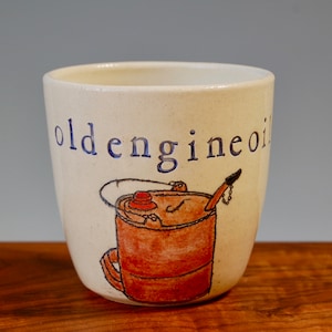 May include: A white ceramic mug with a blue and black inscription that reads "old engine oil". The mug has a hand-painted illustration of an orange oil can with a black spout and a red lid.