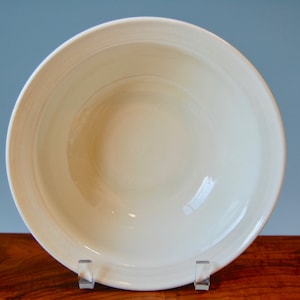 May include: A white ceramic bowl with a smooth, glossy finish. The bowl has a wide, shallow shape and a slightly rounded rim.