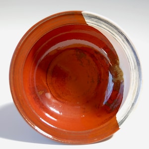 May include: A red ceramic bowl with a white rim and a black stripe. The bowl has a glossy finish and is slightly textured.