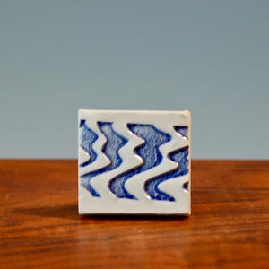 May include: A white ceramic tile with a blue wavy pattern.