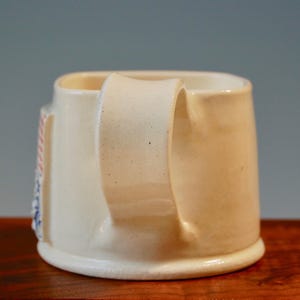 May include: A white ceramic mug with a handle. The mug has a design on the side with red, white and blue stripes.