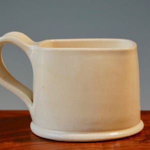 May include: A white ceramic mug with a square shape and a rounded handle.