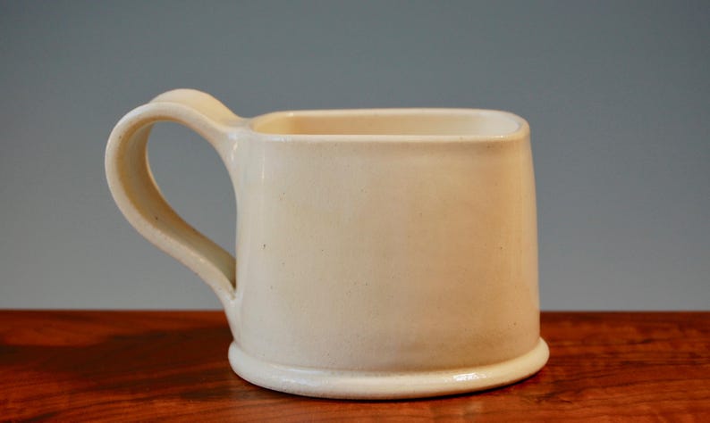 May include: A white ceramic mug with a square shape and a rounded handle.