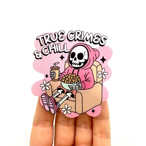 Könnte beinhalten: Ein rosa-weißer Aufkleber mit einem Cartoon-Skelett, das einen rosa Hoodie trägt und eine Schüssel Popcorn und ein Getränk hält. Der Text "TRUE CRIMES & CHILL" befindet sich über dem Skelett.