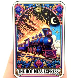 Op de afbeelding: Een vintage-stijl tarotkaart-illustratie van een brandende trein met de tekst "The Hot Mess Express". De trein is blauw en paars met gouden accenten. De achtergrond is een donkerblauwe lucht met sterren en een halve maan.