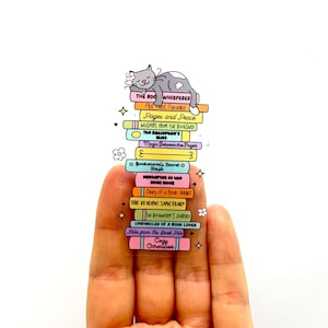 Puede incluir: Una pila de libros coloridos con títulos relacionados con la lectura y los libros. Los libros están apilados en un dedo, con un gato durmiendo en la parte superior de la pila.