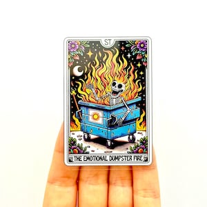 May include: A tarot card depicting a blue dumpster on fire with a skeleton inside. The card is titled "The Emotional Dumpster Fire".
