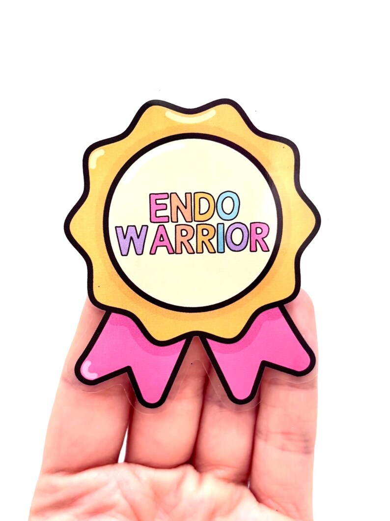 May include: A sticker with the text "ENDO WARRIOR" in a circular design. It has a yellow scalloped border, a light pink ribbon, and a white background. The text is in various colors. A badge of honor.