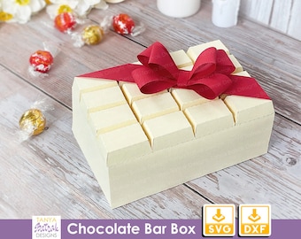 May include: A white chocolate bar box with a red ribbon bow. The box is decorated to look like a chocolate bar. The box is on a wooden surface. The text "Chocolate Bar Box" is printed below the box. The text "SVG" and "DXF" are printed below the text "Chocolate Bar Box".
