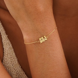Könnte beinhalten: Ein goldenes Kettenarmband mit einem Anhänger, der drei stilisierte Figuren zeigt, die sich an den Händen halten. Der Anhänger ist ein Symbol für Familie und Einheit.