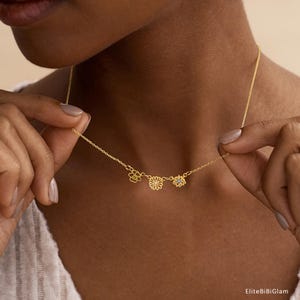 May include: A gold-toned chain necklace featuring three small, distinct flower-shaped charms. The center charm is a daisy design with a small white stone, flanked by two other floral motifs, one with a yellow stone and one with a blue stone.