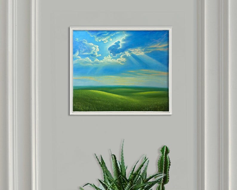 May include: A framed landscape painting depicts a vibrant green field under a bright blue sky with fluffy white clouds. The sun's rays pierce through the clouds, illuminating the scene. The artwork is mounted on a gray wall.