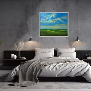 May include: A framed landscape painting depicting a green field under a blue sky with clouds and sun rays. The artwork hangs above a bed with white bedding and a gray blanket. The room has a modern design with gray walls.