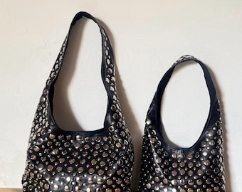 May include: Two black hobo-style shoulder bags of different sizes, both featuring a dense pattern of circular silver-toned metal studs covering the entire exterior surface, including the shoulder straps, with a smooth black leather-like finish.