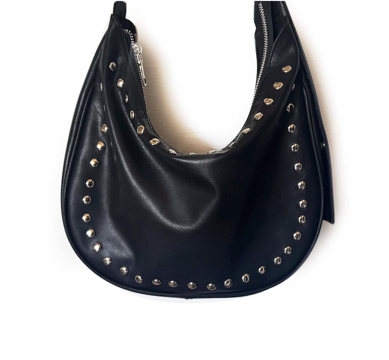 Puede incluir: Un bolso hobo de cuero negro con tachuelas plateadas alrededor de los bordes.