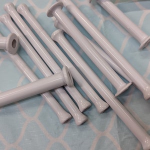 May include: A group of white plastic yarn winding sticks, also known as knitting bobbins, are scattered on a light blue patterned surface.