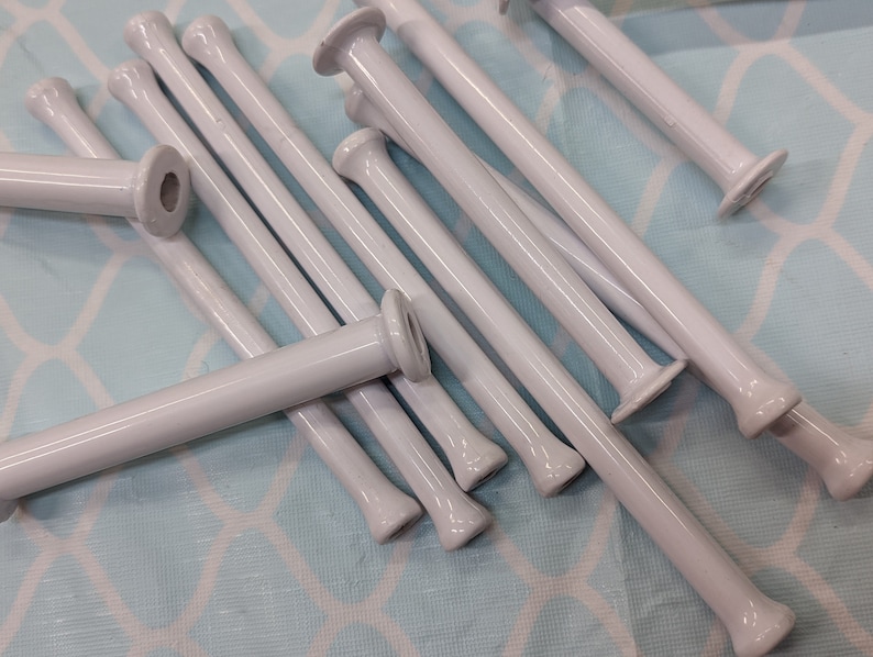 May include: A group of white plastic yarn winding sticks, also known as knitting bobbins, are scattered on a light blue patterned surface.