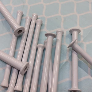 May include: A group of white plastic knitting needles, also known as stitch holders, are arranged on a light blue background. The needles are approximately 6 inches long and have a smooth, rounded tip.