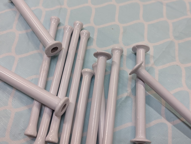 May include: A group of white plastic knitting needles, also known as stitch holders, are arranged on a light blue background. The needles are approximately 6 inches long and have a smooth, rounded tip.