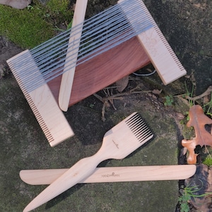 May include: A wooden weaving loom with a gray yarn warp, a wooden needle, a wooden comb, and a wooden tool labeled "Handyman" and "Weaving Tool".