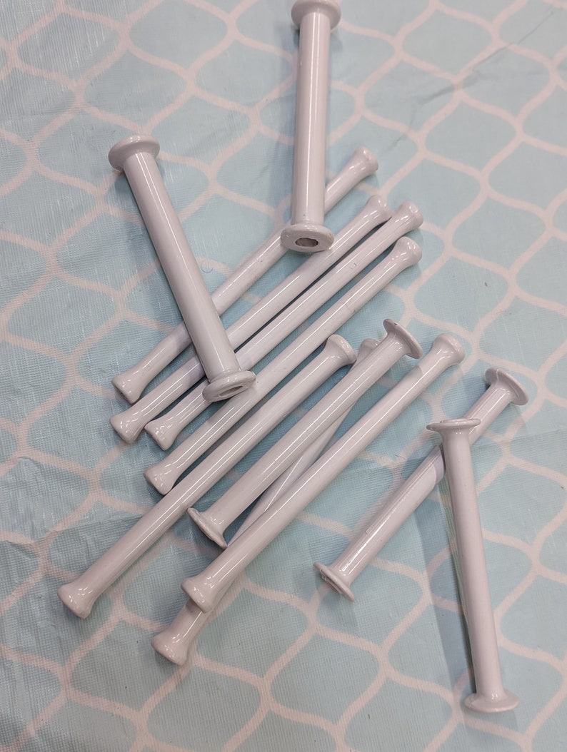 May include: A group of white plastic bobbins for winding yarn. The bobbins are arranged in a random pattern on a light blue background.