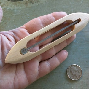 May include: A wooden shuttle with a clear plastic thread guide. The shuttle is about the size of a US quarter.