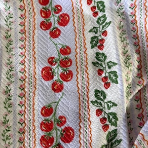 May include: Textile featuring a repeating pattern of red tomatoes and green leaves on a pale blue backdrop. Vertical stripes with pink flowers and orange lines border the tomato and strawberry designs.