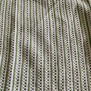 May include: Close-up of a textured fabric with a striped pattern. The fabric features alternating vertical stripes of white and green. The weave creates a grid-like appearance with small rectangular openings throughout the material.