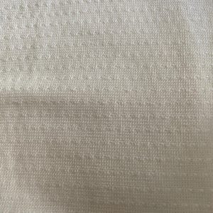May include: Close-up of a textured, off-white fabric. The material has a woven appearance with a subtle, repeating pattern of small, raised squares. The overall texture is soft and inviting, suggesting a comfortable textile.