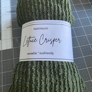 May include: An olive green Lettuce Crisper made of textured fabric, rolled up and ready for use. A white label wrapped around the crisper reads "HANDMADE Lettuce Crisper reusable * ecofriendly" in black script.