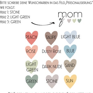 Op de afbeelding: Een kleurenkaart met hartvormen. De kleuren zijn perzik, taupe, lichtblauw, roze, poederroze, blauw, lichtgroen, donker nude, zand, groen, steen en zon. De tekst "mom of" staat boven de kleurenkaart. De tekst "Bitte schreibe deine Wunschfarben in das Feld, Personalisierung" staat bovenaan de kleurenkaart. De tekst "Wie folgt: Herz 1: Stone Herz 2: Light Green Herz 3: Green" staat onder de tekst "Bitte schreibe deine Wunschfarben in das Feld, Personalisierung". De tekst "Die Farben stammen aus der gleichen Farbpalette und sehen kombiniert wundersch&ouml;n miteinander aus." staat onderaan de kleurenkaart.