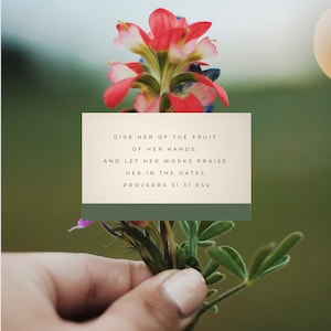 May include: A hand holding a bunch of pink and green wildflowers with a quote from Proverbs 31:31 ESV: "Give her of the fruit of her hands, and let her works praise her in the gates."