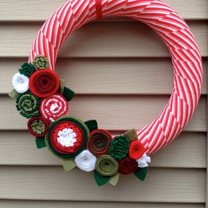 May include: A red and white striped wreath decorated with felt flowers in shades of red, green, and white.