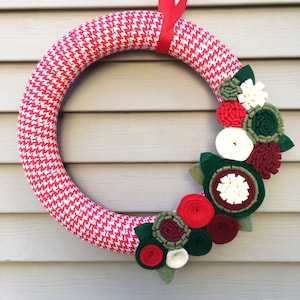 May include: A red and white houndstooth patterned wreath with a red ribbon and a cluster of felt flowers in shades of red, white, and green.