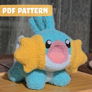 May include: A handmade plush toy in the shape of a cartoon creature, mainly blue with yellow cheek accents and a pink nose. The text "PDF PATTERN" is displayed in a yellow banner above the toy.