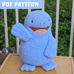 May include: A light blue plush toy with a textured, fuzzy surface, featuring a wide brown mouth and a pink tongue. The creature has a rounded body, two small arms with one raised, and two flat feet. The text PDF PATTERN is visible at the top.