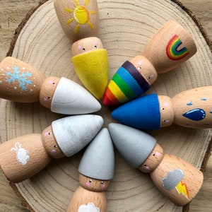 May include: A set of nine wooden gnome ornaments painted with different weather themes. The gnomes are painted with a sun, rainbow, snowflake, clouds, rain, a storm cloud, and a gray sky.