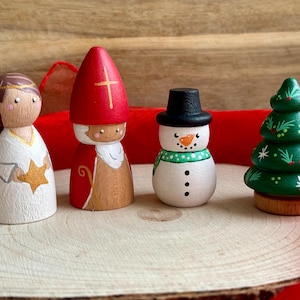 Könnte beinhalten: Holz-Weihnachtsfiguren, darunter ein Engel, Nikolaus, ein Schneemann und ein Weihnachtsbaum. Der Engel hält einen Stern, Nikolaus trägt einen roten Hut, der Schneemann hat einen schwarzen Hut und Schal, und der Baum ist grün.