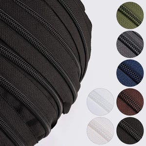 May include: Close-up of a roll of black zippers, showcasing the teeth and fabric detail. The image also includes color swatches of zippers in olive green, gray, navy blue, white, brown, and black. Ideal for sewing and crafting projects.
