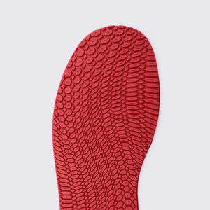May include: Close-up of a red shoe sole with a textured, honeycomb-like pattern. The sole is a vibrant red color and has a curved shape, suggesting it is for a shoe. The pattern is detailed and covers the entire surface.