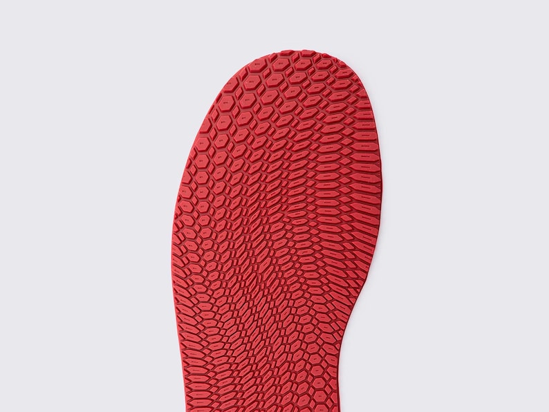 May include: Close-up of a red shoe sole with a textured, honeycomb-like pattern. The sole is a vibrant red color and has a curved shape, suggesting it is for a shoe. The pattern is detailed and covers the entire surface.