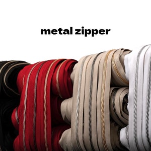May include: Close-up of several rolls of metal zippers in various colors, including black, red, beige, and white. The text "metal zipper" is displayed above the zippers. The zippers have metallic teeth and are tightly rolled.