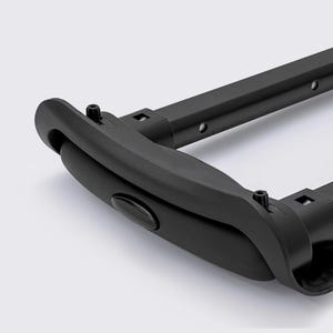 May include: Close-up of a black luggage handle with a curved grip and rectangular frame. The handle has a button and is attached with screws. The frame has several holes and square openings.